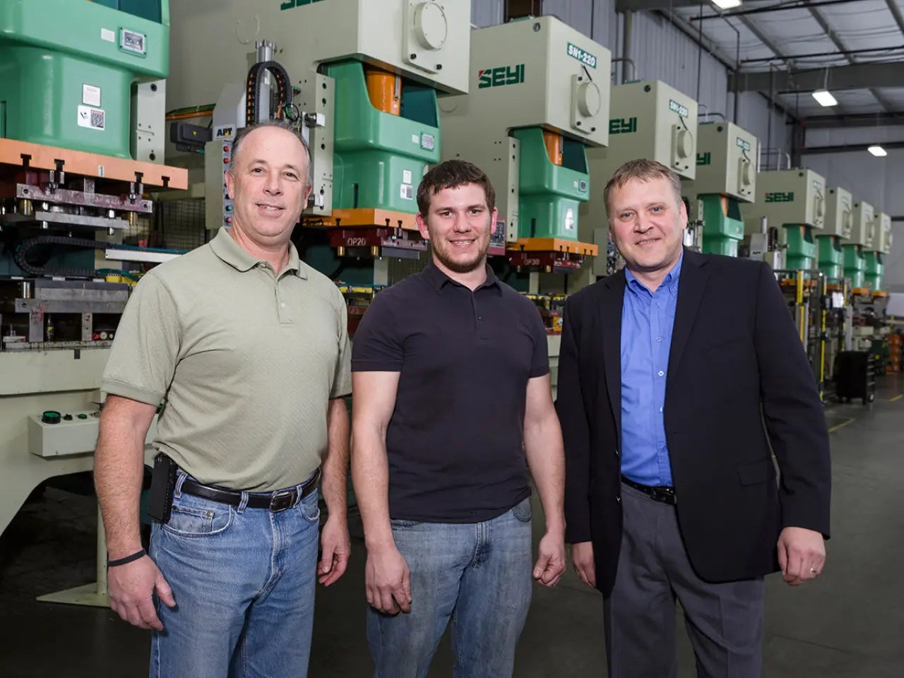 Das Team von Great Lakes Metal Stamping neben einer Presse.